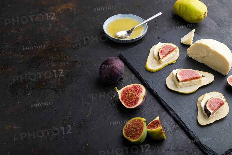 Summer appetizer with pear, cottage cheese, figs and honey on slate board on a black concrete background. Side view, copy space