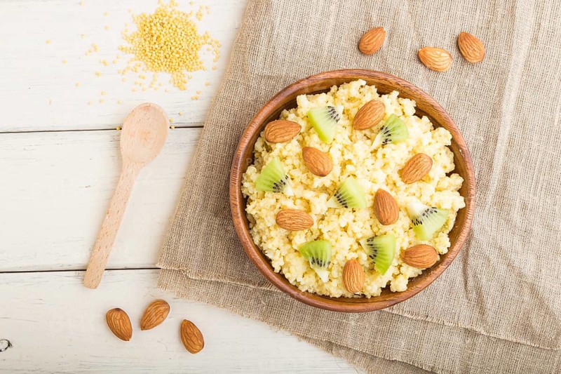 Millet porridge with kiwi and almonds in wooden bowl on a white wooden background and linen textile. Top view, flat lay, close up