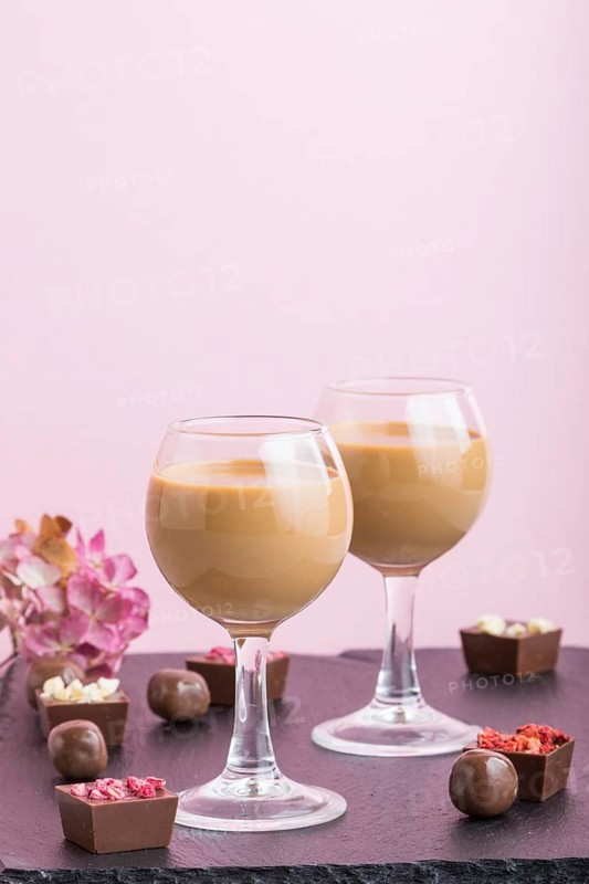 Sweet chocolate liqueur in glass with chocolate candies on a pink background and black stone slate board. Side view, close up, copy space