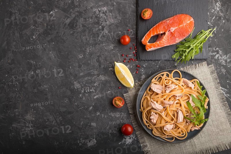 Semolina pasta with salmon and salmon steak on a black concrete background and linen textile. Top view, flat lay, copy space
