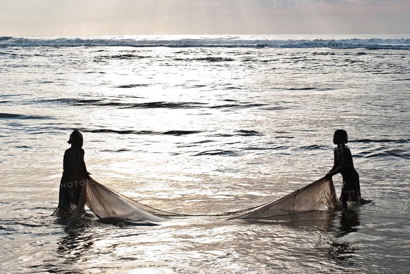 Silhouette of two girls fishing bichiques on the Indian ocean coast, Mananjary, Madagascar. Bichiques are fry of two species of freshwater fish belonging to the family gobiidae