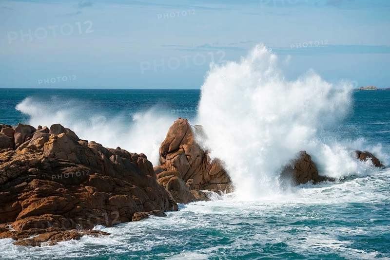 Dramatic waves crashing against rocks in a blue ocean under a clear sky, Ploumanac'h, Ploumanach, Perros-Guirec, Côtes-d'Armor, Brittany, France, Europe