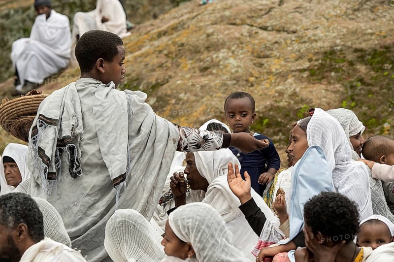 Altar boy distributes blessed bread to worshippers in traditional white Shamma dress after the Sunday service, Lalibela, Ethiopia, Africa