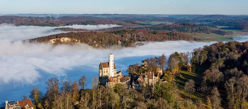 Sunshine in the mountains, fog in the Echaz valley. Lichtenstein Castle in the Swabian Alb. The fairytale castle of Württemberg is a 19th century castle built in the historicist style. Aerial view, panoramic photo. Lichtenstein, Baden-Württemberg, Germany, Europe