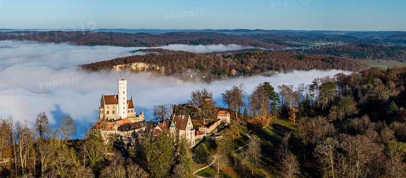 Sunshine in the mountains, fog in the Echaz valley. Lichtenstein Castle in the Swabian Alb. The fairytale castle of Württemberg is a 19th century castle built in the historicist style. Aerial view, panoramic photo. Lichtenstein, Baden-Württemberg, Germany, Europe