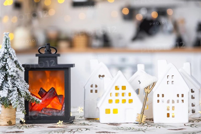 Key and tiny house of a small size on cozy home with Christmas decor on table of festive white kitchen. Gift for New Year. Insurance, moving to new house, mortgage, rent and purchase real estate