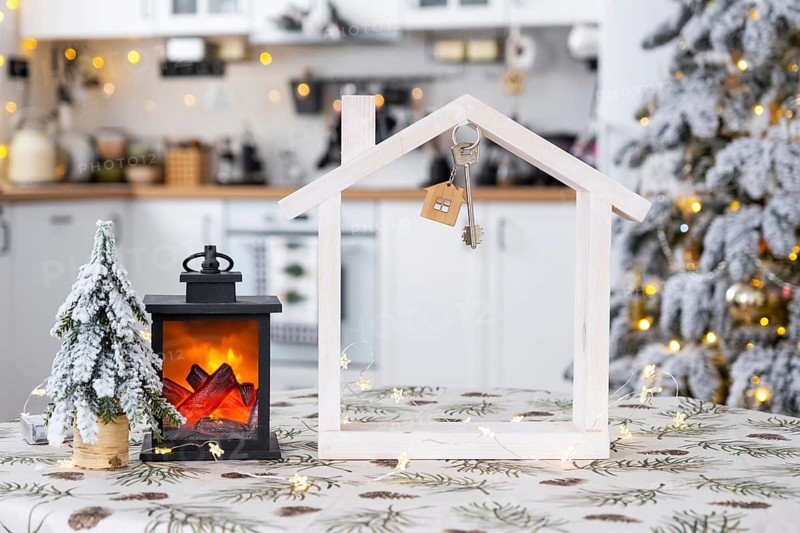 Key and tiny house of a small size on cozy home with Christmas decor on table of festive white kitchen. Gift for New Year. Insurance, moving to new house, mortgage, rent and purchase real estate