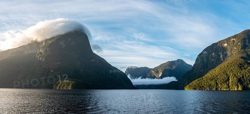 Sun rising over Doubtful Sound, Clouds hanging low on the mountains, South Island of New Zealand