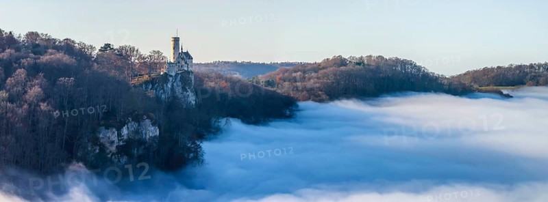 Sunshine in the mountains, fog in the Echaz valley. Lichtenstein Castle in the Swabian Alb. The fairytale castle of Württemberg is a 19th century castle built in the historicist style. Aerial view, panoramic photo. Lichtenstein, Baden-Württemberg, Germany, Europe
