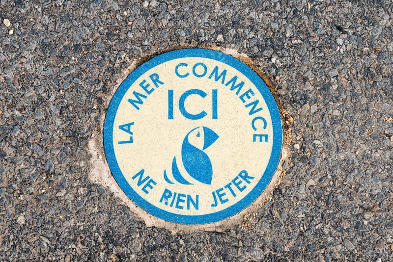 Round blue sticker on the road with fish symbol and environmental message, the sea begins here, don't throw anything away here, Ploumanac'h, Ploumanach, Côte d'Armor, Brittany, France, Europe
