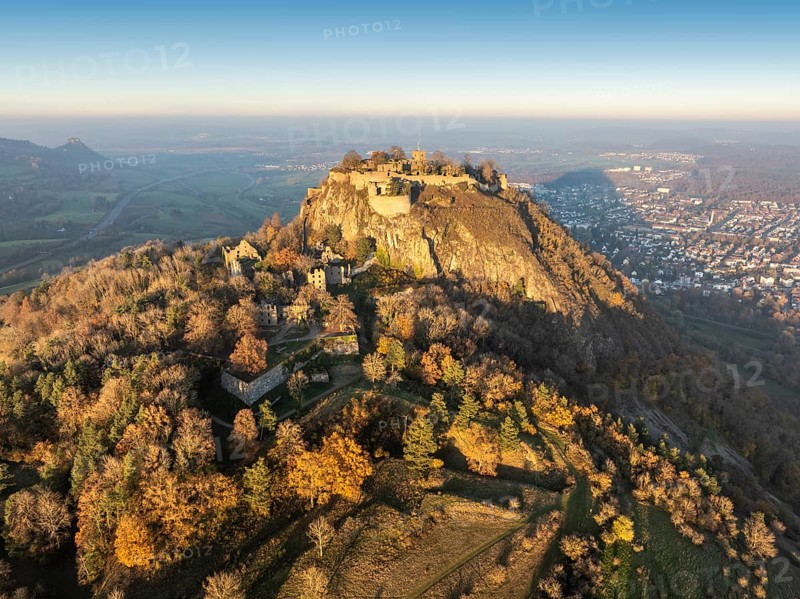 Aerial view of the volcanic cone Hohentwiel with the castle ruins illuminated by the evening sun, behind it the town of Singen am Hohentwiel, on the left on the horizon the Hohenkrähen, Singen am Hohentwiel, district of Constance, Baden-Württemberg, Germany, Europe