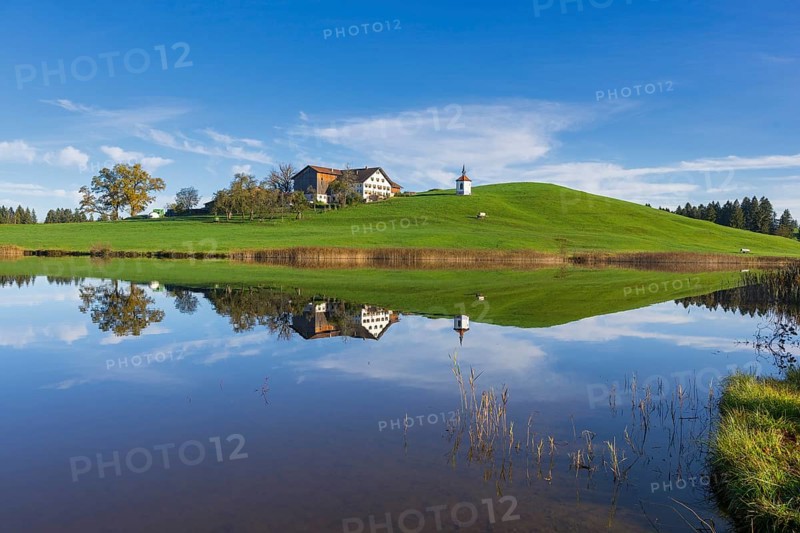 View of a lake with reflection of a house and a chapel on a hill, Hegratsrieder See near Füssen, Ostallgäu, Bavaria, Germany, Europe