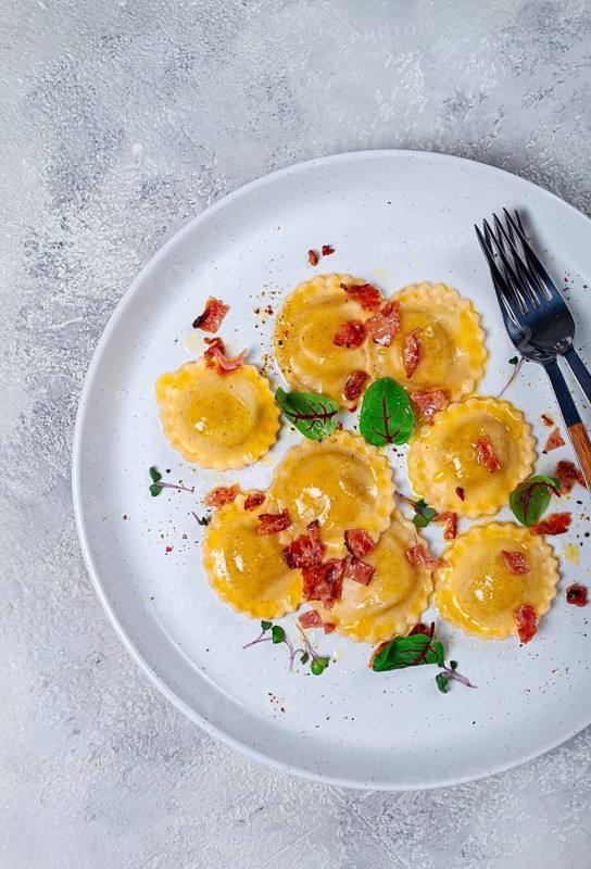 Fresh ravioli, with butter, spices and herbs, fried bacon, on the table, top view, light background, no people