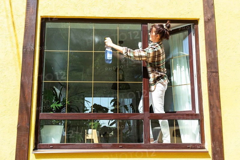 A woman manually washes the window of the house with a rag with a spray cleaner and a mop outside. Safety at height, restoring order and cleanliness in the spring, cleaning service