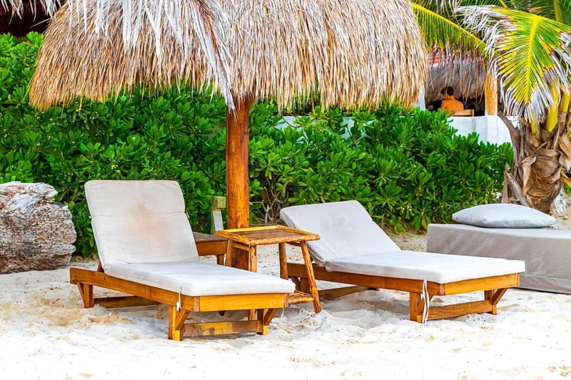 Palapa thatched roofs palm trees parasols umbrellas and sun loungers at the beach resort hotel on tropical mexican beach in Playa del Carmen Mexico