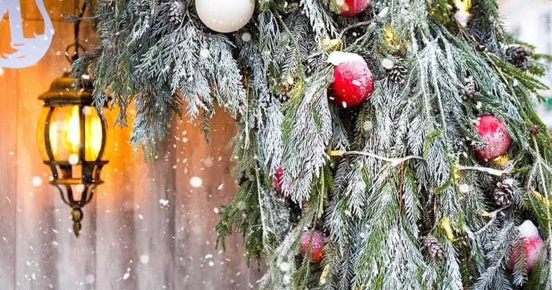 Outdoor Christmas decorations made of natural spruce branches, toys, garlands and a glowing lantern in the snow in a blizzard. Winter outside, snowfall. New Year decor