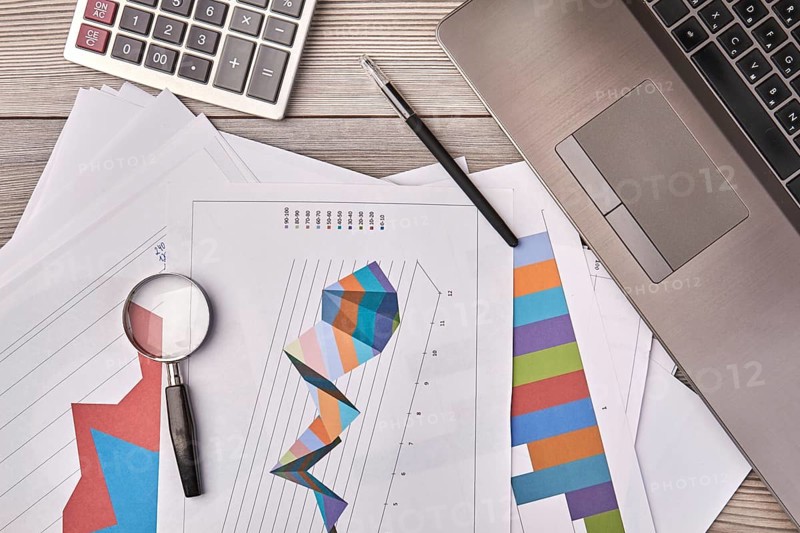Papers with charts and glass magnifier with pen. Laptop device with calculator top view