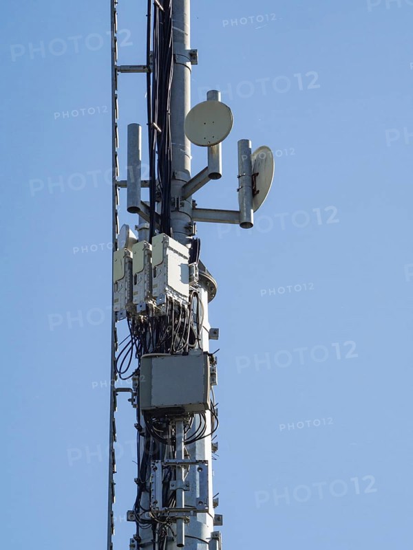 Telecommunication tower against a clear blue sky, featuring antennas, microwave dishes, and electronic equipment, symbolizing modern communication infrastructure