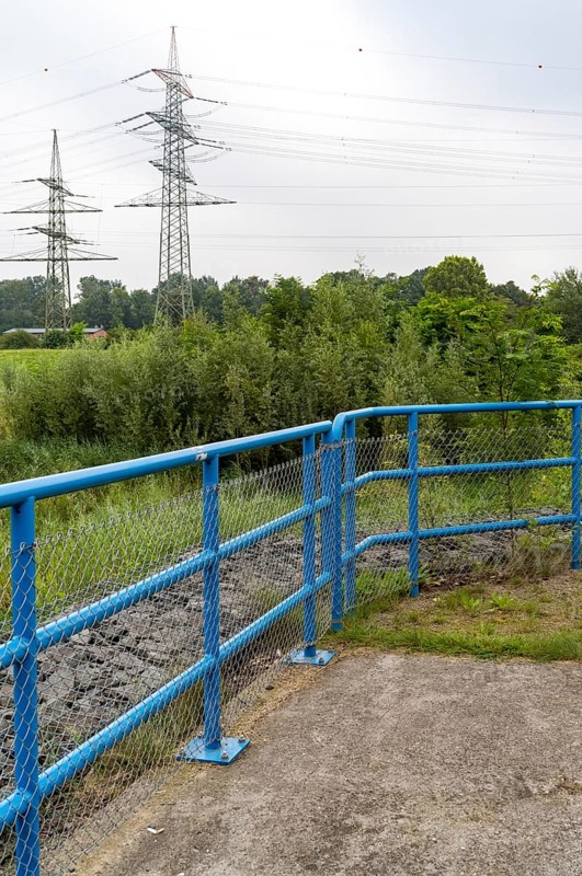 Blue metal railing in front of high voltage pylons
