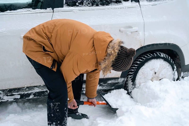 A man digs out a stalled car in the snow with a car shovel. Transport in winter got stuck in a snowdrift after a snowfall, sat on the bottom. First aid, tow truck, winter tires spikes and all-season