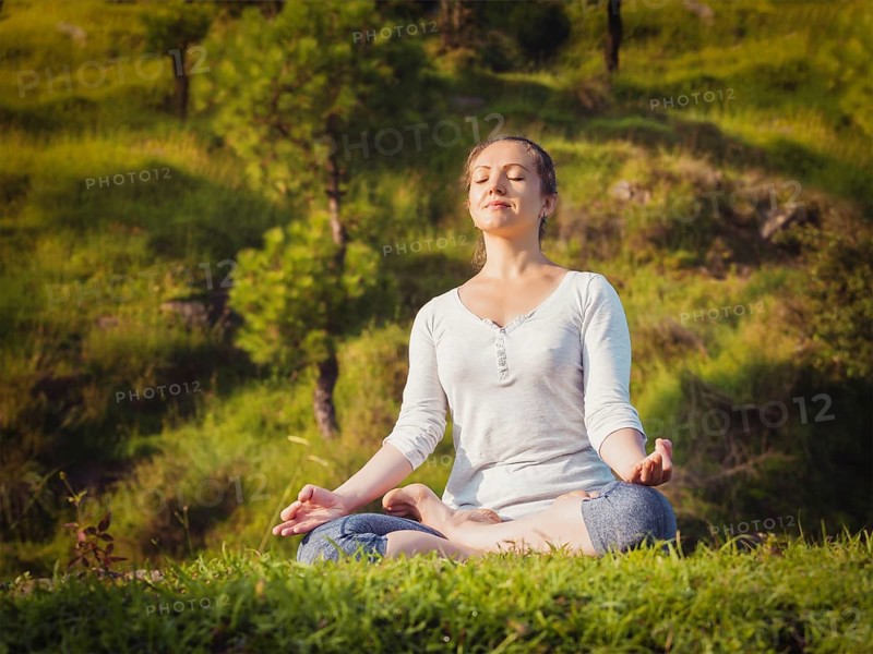 Young sporty fit woman doing yoga outdoors, meditating and relaxing in Padmasana Lotus Pose) with chin mudra on green grass in forest. Vintage retro effect filtered hipster style image
