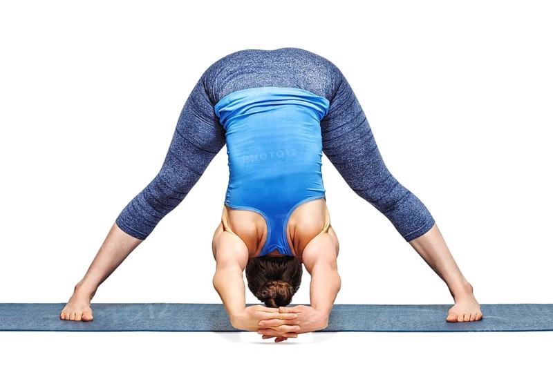 Beautiful sporty fit woman practices Ashtanga Vinyasa yoga asana Prasarita padottanasana C, wide legged forward bend C isolated on white