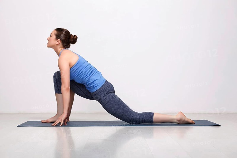 Beautiful sporty fit yogini woman practices yoga asana Anjaneyasana, low crescent lunge pose in surya namaskar in studio