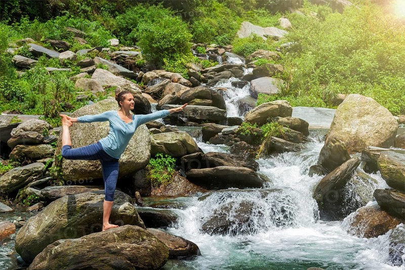 Yoga outdoors, woman doing yoga asana Natarajasana, Lord of the dance balance pose outdoors at waterfall in Himalayas
