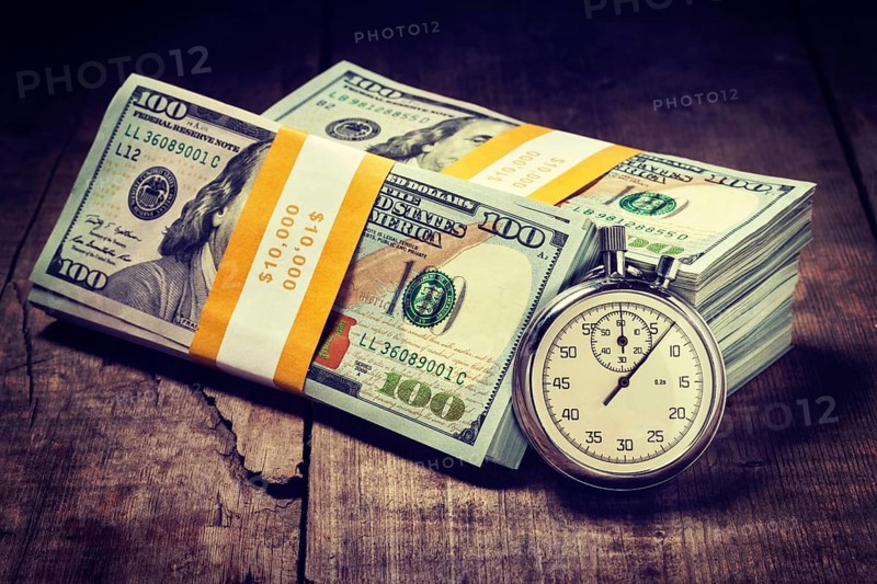 Time is money loan concept background. Vintage retro effect filtered hipster style image of stopwatch and stack of new 100 US dollars 2013 edition banknotes bills bundles on wooden background