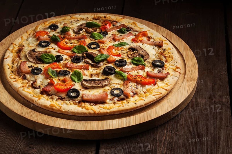 Ham pizza with (capsicum), mushrooms, olives and basil leaves on wooden board on old table