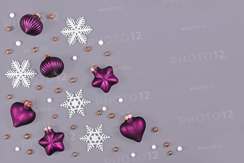 Christmas flat lay with purple heart and star shaped and round tree ornament baubles and white snowflakes on gray background with empty copy space on side