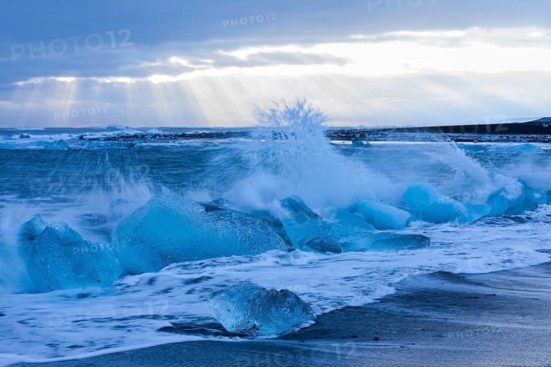 Waves breaking on icebergs on the black beach of Breidamerkursandur, near Jökullsarlon, Sudurland, Iceland, Europe