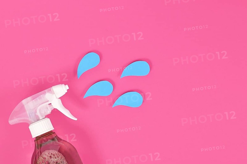 Cleaning agent spray bottle with blue liquid drops cut from paper on pink background