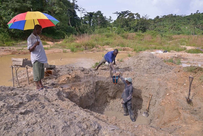 Diamond hunters digging a pit with shovels, supervisor holding a parasol, left, near Koidu, Koidu-Sefadu, Kono District, Eastern Province, Sierra Leone, Africa