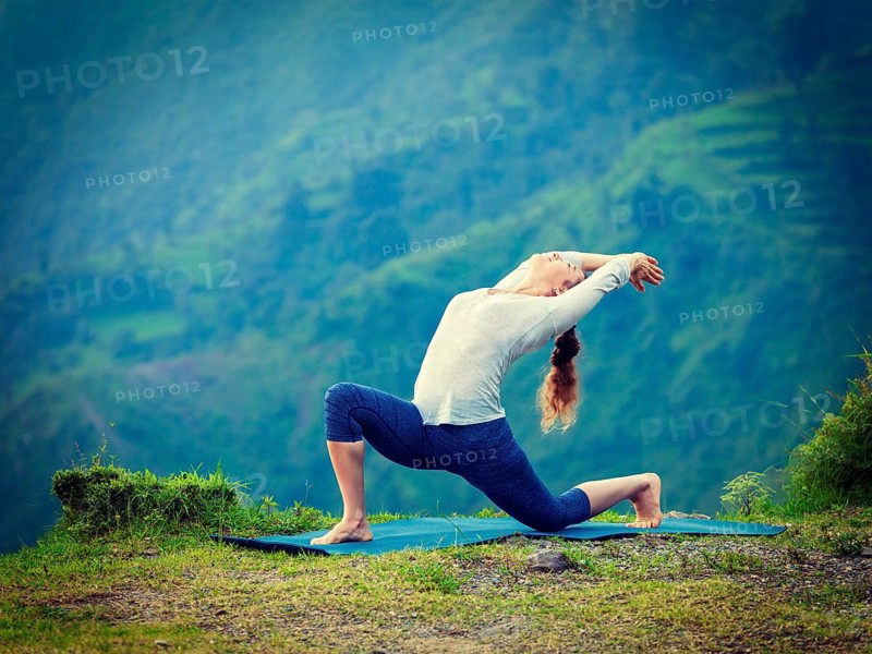 Yoga outdoors, sporty fit woman practices Hatha yoga asana Anjaneyasana, low crescent lunge pose posture outdoors in Himalayas mountains. Vintage retro effect filtered hipster style image