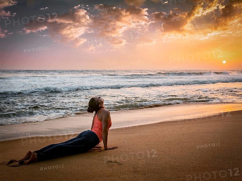 Yoga outdoors, woman doing Ashtanga Vinyasa yoga Surya Namaskar Sun Salutation asana Urdhva Mukha Svanasana, upward facing dog pose on sunset on beach. Vintage retro effect filtered hipster style image