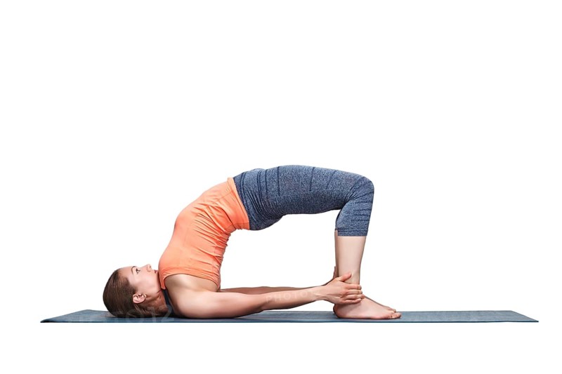Beautiful sporty fit yogini woman practices yoga asana setu bandhasana, bridge pose advanced variation in studio isolated on white