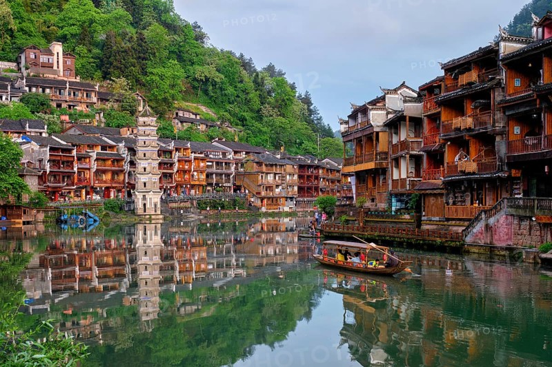 Chinese tourist attraction destination, Feng Huang Ancient Town (Phoenix Ancient Town) on Tuo Jiang River with Wanming Pagoda tower and tourist boat on sunset. Hunan Province, China, Asia