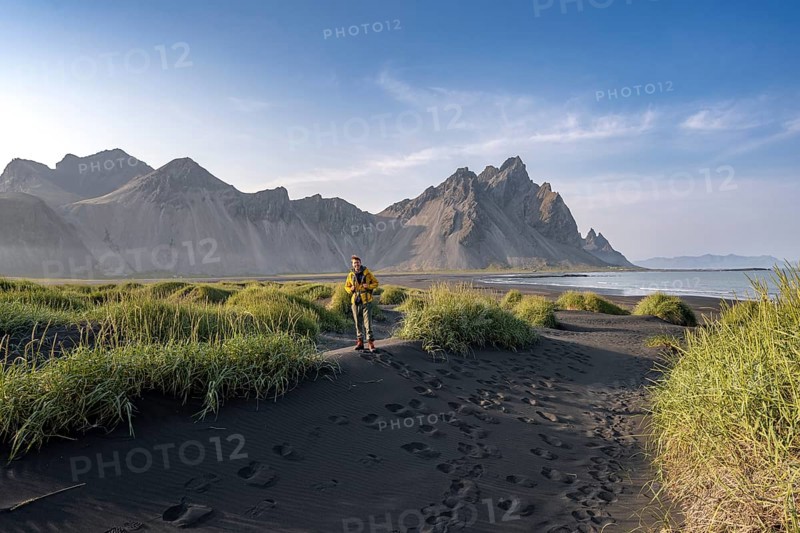 Tourist on a sand dune, Black beach with volcanic sand, Sand beach, Dunes with grass, Stokksnes headland, Klifatindur mountain range, Austurland, East Iceland, Iceland, Europe