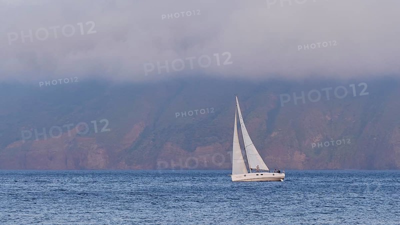 Single sailing boat, lying diagonally in the water, lusts of Lipari, low-hanging clouds, Lingua, south-eastern tip of the island, Salina, Aeolian Islands, Lipari Islands, Sicily. Italy