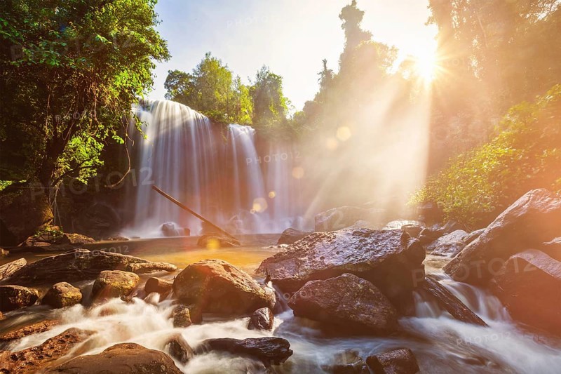 Tropical waterfall in the morning with sun rays in Cambodia. Lens flare and light leak