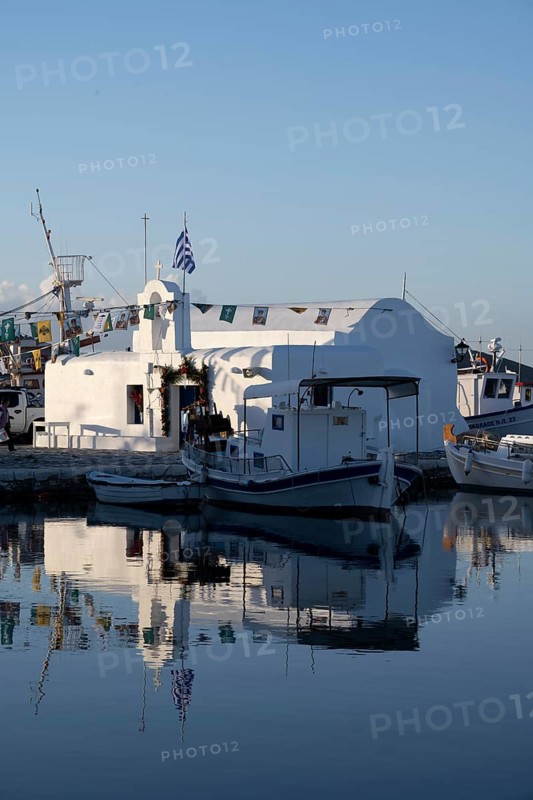 White Cycladic Greek orthodox church Agios Nikolaos, decorated with flags, harbour of Naoussa, reflected in the water, Naoussa, Paros, Cyclades, Greece, Europe