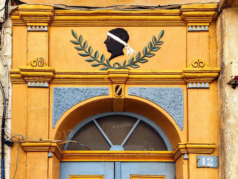 Colourful house entrance, decorated front door, black head with white headband, traditional symbol of the freedom struggle of the Corsicans, tête de maure, detail, old town of L'Île-Rousse, Ile Rousse, Corsica, France, Europe