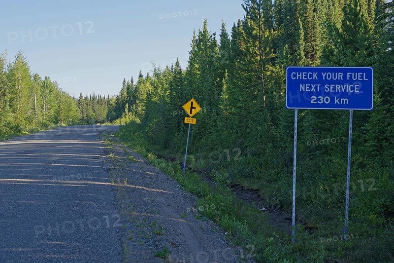 Narrow, traffic-free road and a sign pointing to the next petrol station, mountain landscape, wilderness, Stewart Cassiar Highway, British Columbia, Canada, North America