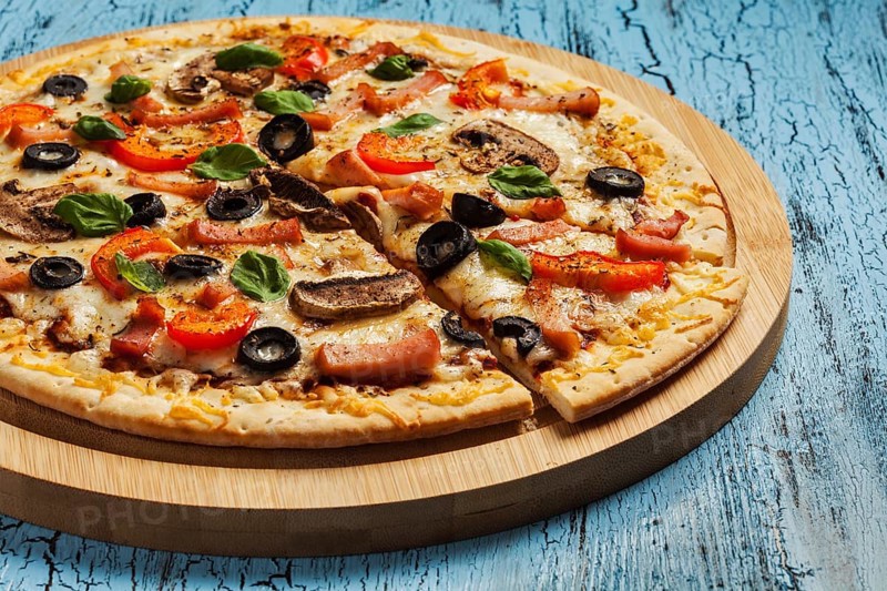 Ham pizza with (capsicum), mushrooms, olives and basil leaves on wooden board on blue table