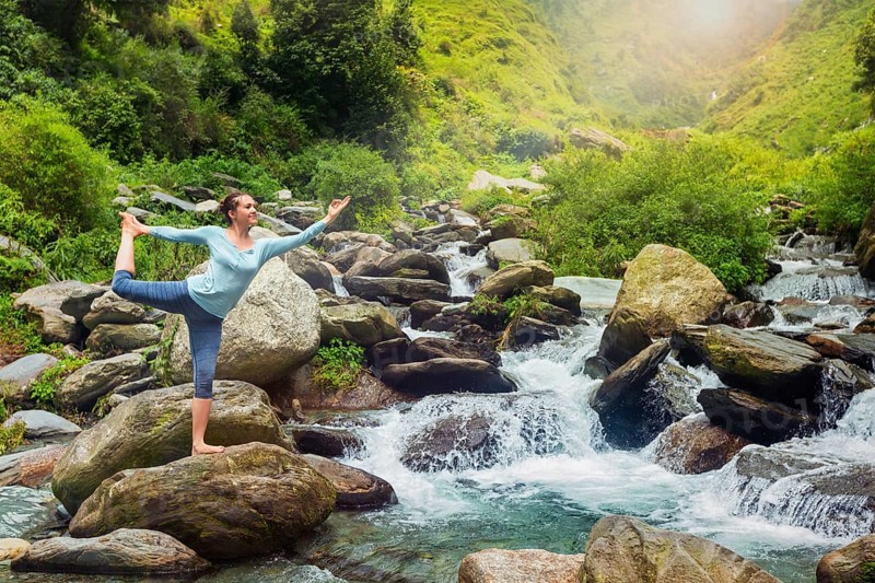 Yoga outdoors, woman doing yoga asana Natarajasana, Lord of the dance balance pose outdoors at waterfall in Himalayas