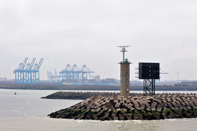 Pier with signal light at the port entrance and container terminal cranes of the port of Zeebrugge, Belgium, Europe