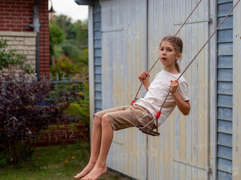 Boy swinging while sitting on children's swing at shed and garden gate, Germany, Europe