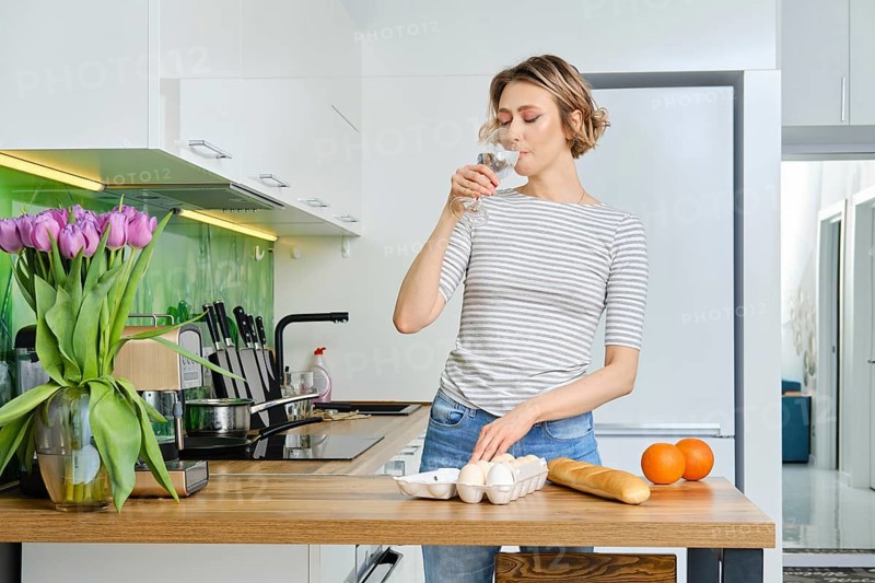 Beautiful young woman drinks water before making breakfast in her kitchen