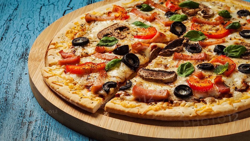 Panorama of ham pizza with (capsicum), mushrooms, olives and basil leaves on wooden board on blue table